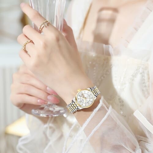 Close-up of a woman's hand wearing a watch and rings, holding a glass.