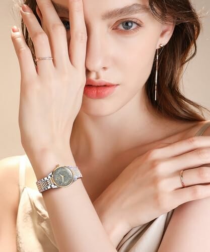 Woman posing with hand on face, wearing a stylish watch and earrings.
