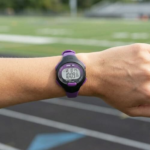 Person wearing a purple digital wristwatch on a running track.